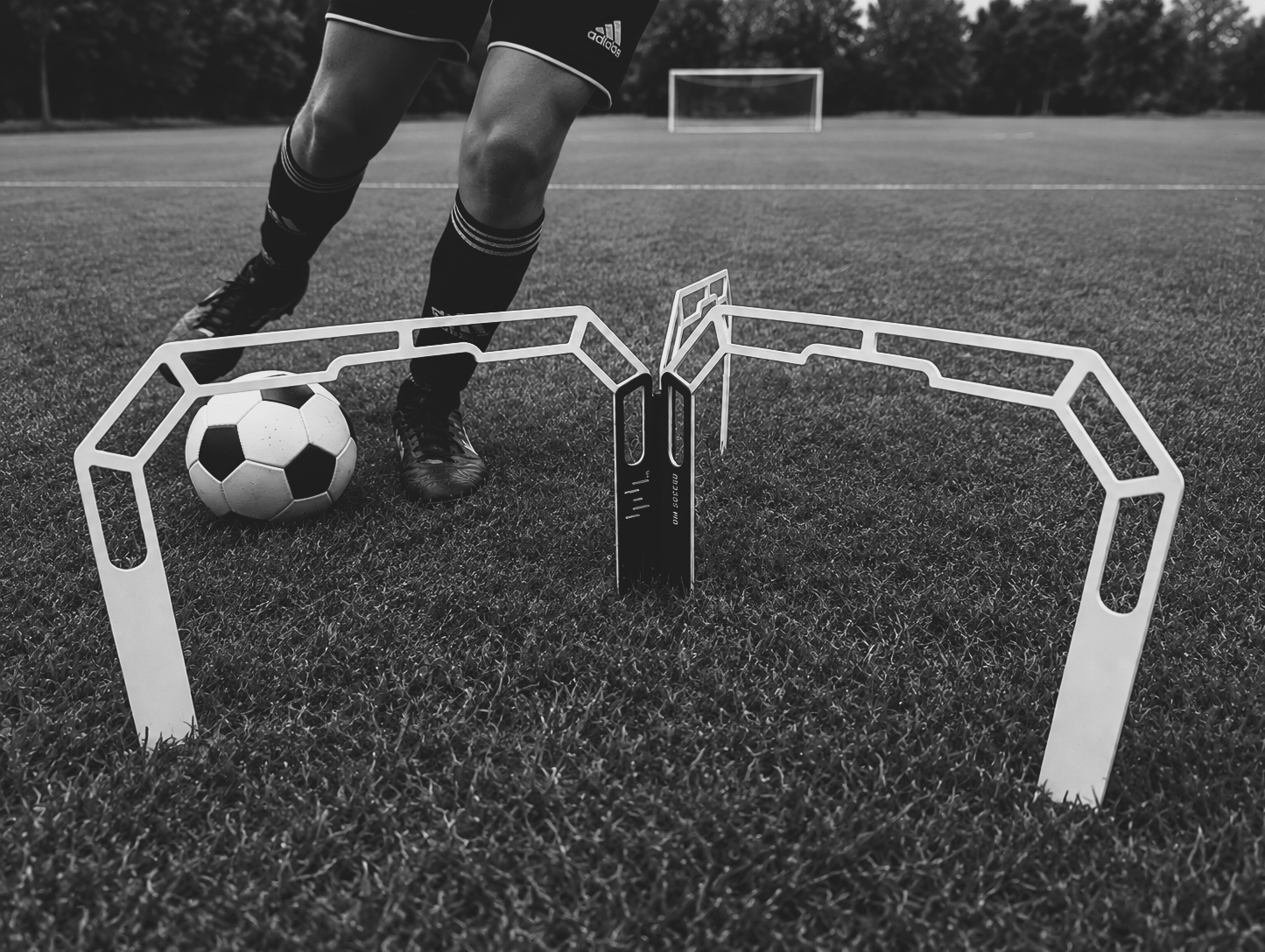 A player dribbling a soccer ball through the OM Trainer on a grass field