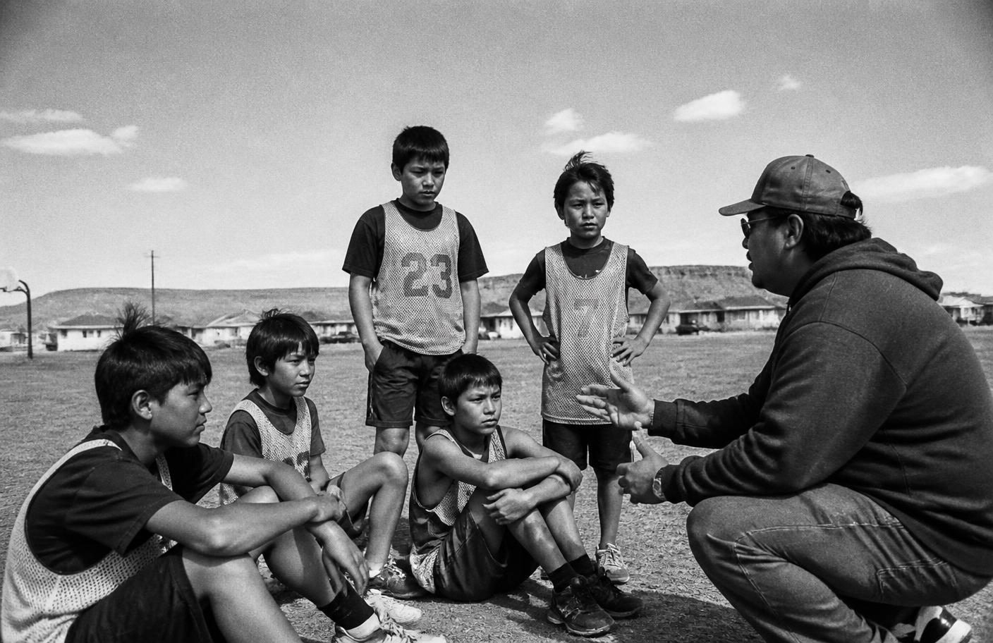 Coach speaking with a group of young athletes on a field in a remote community