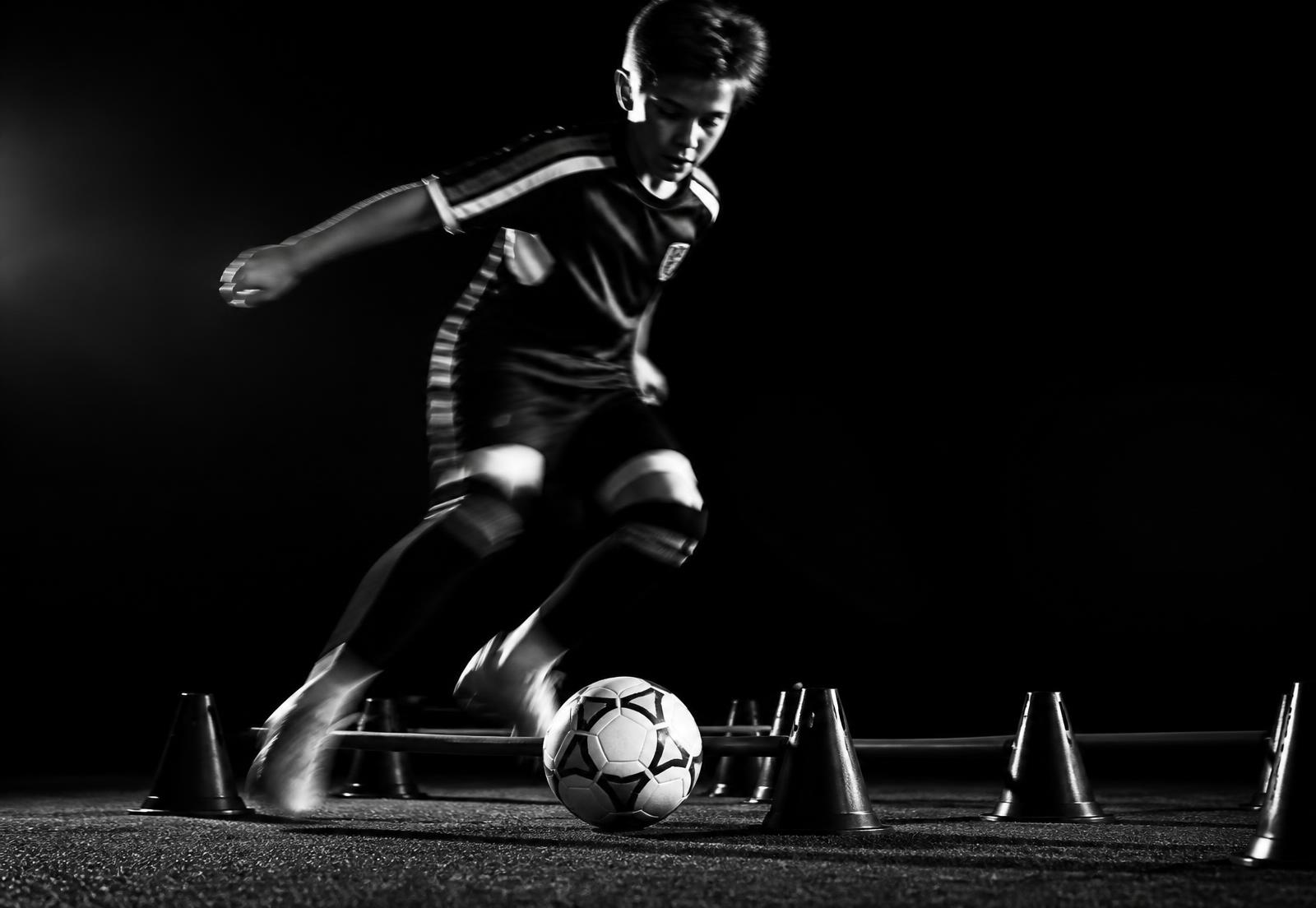 Young player dribbling through tight obstacle equipment in dramatic black and white light
